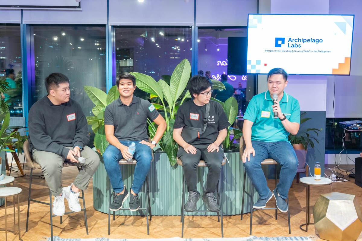 Five speakers seated for a panel discussion in front of the Archipelago Labs presentation screen